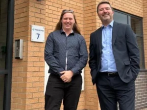 Two men stood in front of a building posing for a photo